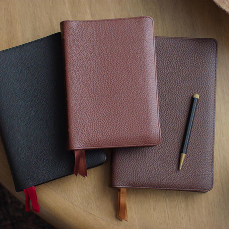 Stack of leather ESV Heirloom Bibles with a pen on a wooden table