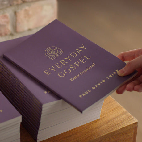 Purple book titled 'Everyday Gospel' held by a hand on a wooden surface.