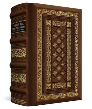 A luxury leather-bound Bible shown at a three-quarter angle on a white background. The cover is dark brown leather with ornate gold foil detailing, and a black title label is visible on the spine.