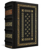 A black leather-bound book with ornate gold foil detailing on the cover and spine, featuring a brown label on the upper spine